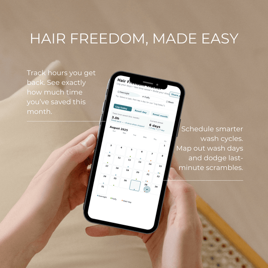 Close-up of a woman’s hand holding a smartphone displaying the Hair Freedom Tracker calendar—today is highlighted and colored dots show Overnight/Fluffy/Wash logs.